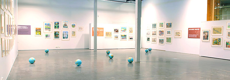 Vaalea näyttelytila, jonka seinillä on teoksia. Lattialla on kahdeksan noin jalkapallon kokoista maapalloa